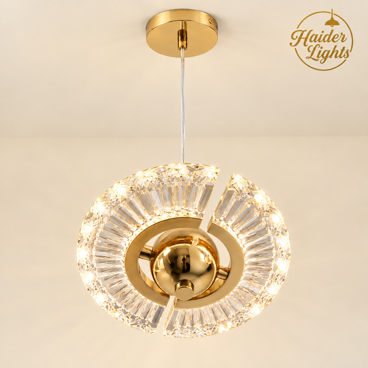 A modern circular chandelier pendant light with a gold-finished ceiling canopy and central hub, surrounded by clear faceted crystal prisms and illuminated by warm white LED lights. The brand logo 'Haider Lights' is visible in the top right corner.